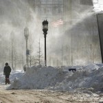 A person walks a dog past plowed snow as wind-whipped snow swirls in Boston's Seaport district on Friday, Jan. 5, 2018, following Thursday's snowstorm. Frigid temperatures, some that could feel as cold as minus 30 degrees, moved across the East Coast on Friday as the region attempted to clean up from a massive winter storm that brought more than a foot of snow, hurricane-force winds and coastal flooding a day earlier. (AP Photo/Bill Sikes)